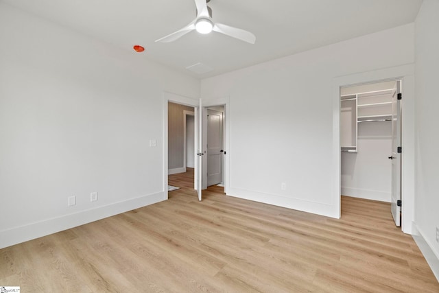 unfurnished bedroom featuring a spacious closet, light hardwood / wood-style flooring, a closet, and ceiling fan