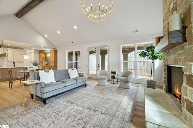 living room featuring a stone fireplace, high vaulted ceiling, beamed ceiling, light hardwood / wood-style floors, and french doors