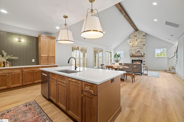 kitchen with sink, hanging light fixtures, a kitchen island with sink, stainless steel dishwasher, and light hardwood / wood-style floors