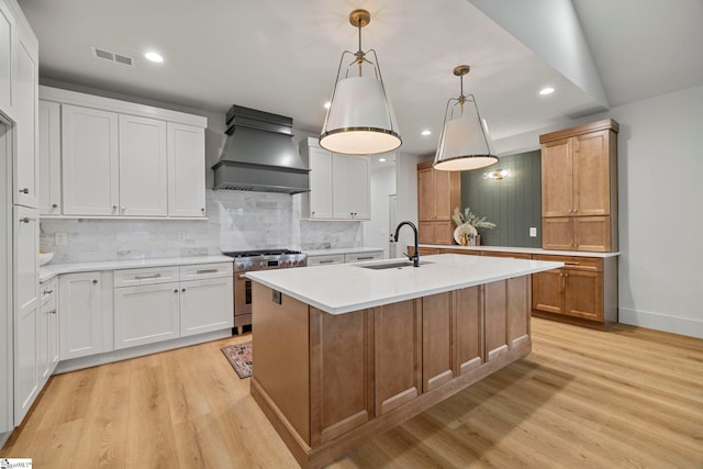 kitchen with white cabinetry, an island with sink, stainless steel stove, and hanging light fixtures