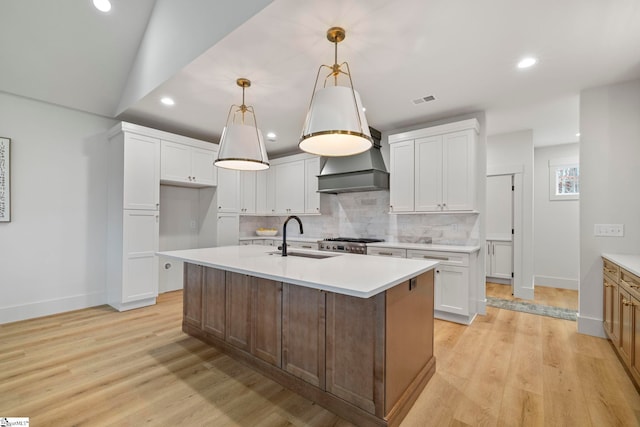 kitchen featuring pendant lighting, custom exhaust hood, an island with sink, and white cabinets