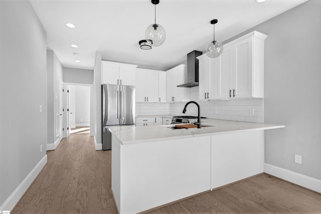 kitchen featuring white cabinetry, wall chimney range hood, stainless steel refrigerator, and kitchen peninsula