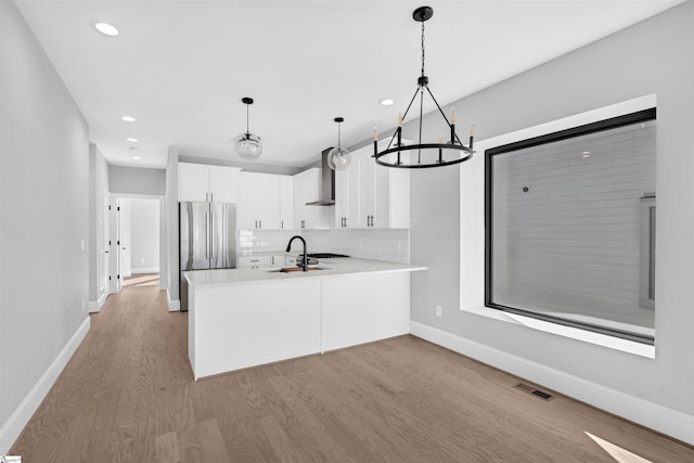 kitchen featuring stainless steel fridge, white cabinetry, light hardwood / wood-style floors, decorative light fixtures, and kitchen peninsula