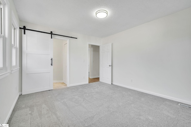 unfurnished bedroom featuring a barn door, light carpet, a textured ceiling, and a closet