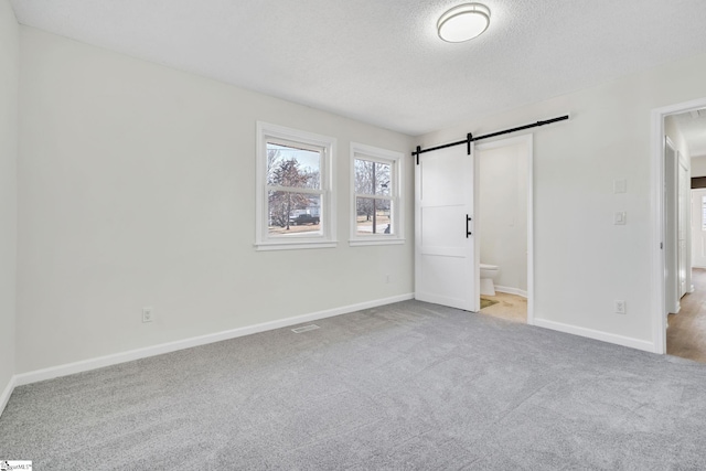 unfurnished bedroom featuring light carpet, connected bathroom, a barn door, and a textured ceiling