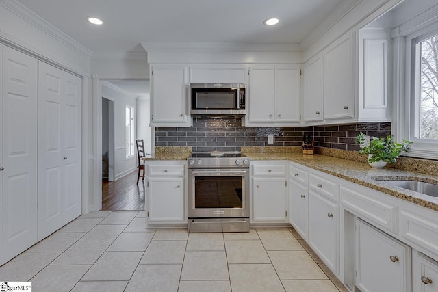 kitchen featuring appliances with stainless steel finishes, white cabinetry, plenty of natural light, light stone countertops, and ornamental molding