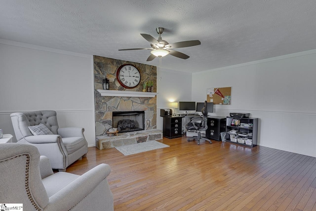 living room with a fireplace, hardwood / wood-style flooring, ceiling fan, crown molding, and a textured ceiling