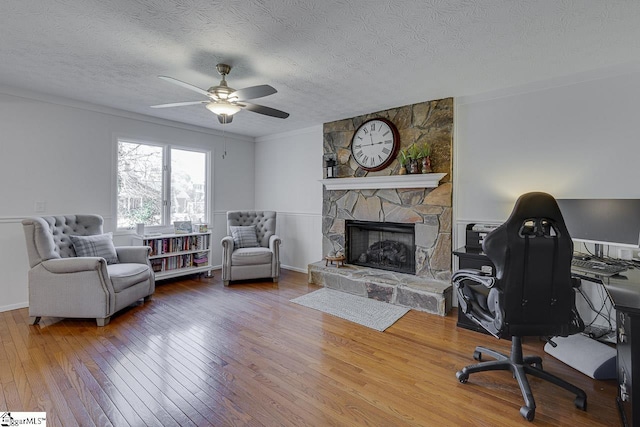 office area featuring ceiling fan, a stone fireplace, hardwood / wood-style floors, and a textured ceiling