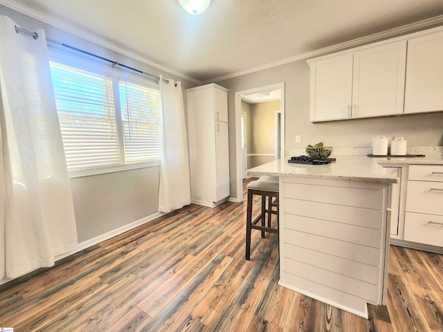 kitchen with white cabinets, a kitchen bar, light stone counters, crown molding, and dark wood-type flooring