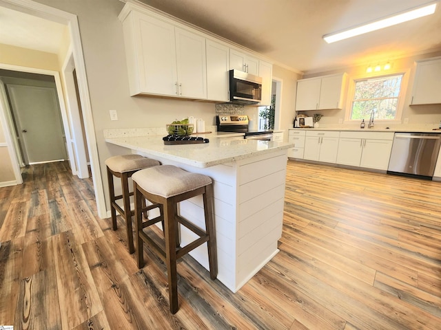 kitchen with light hardwood / wood-style floors, a breakfast bar, white cabinets, and appliances with stainless steel finishes