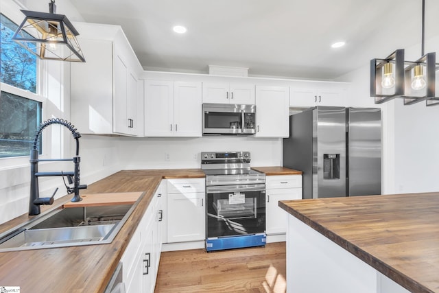 kitchen featuring white cabinetry, wooden counters, stainless steel appliances, and decorative light fixtures