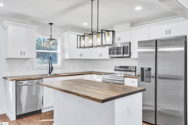 kitchen featuring wooden counters, stainless steel appliances, white cabinets, a kitchen island, and decorative light fixtures