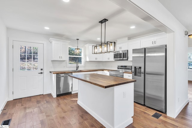 kitchen featuring wood counters, decorative light fixtures, white cabinetry, a center island, and stainless steel appliances