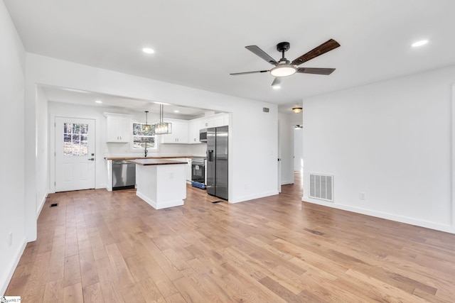 kitchen featuring white cabinetry, hanging light fixtures, stainless steel appliances, a center island, and light wood-type flooring