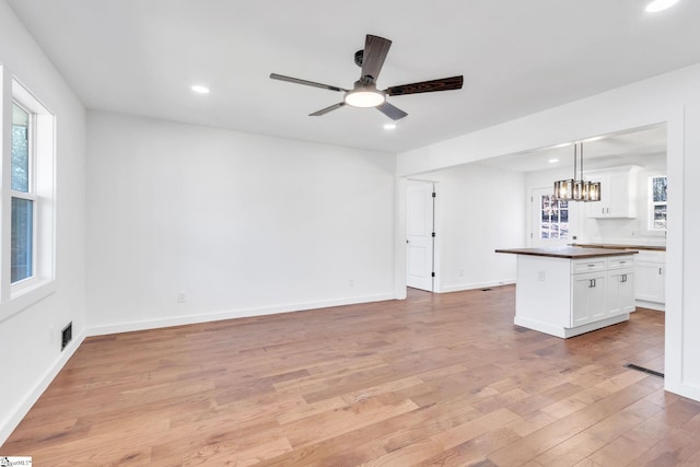 unfurnished living room with ceiling fan with notable chandelier and light hardwood / wood-style flooring