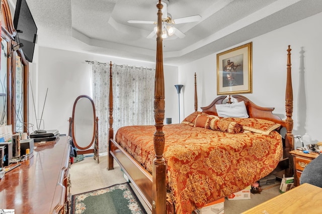 bedroom with ceiling fan, carpet floors, a textured ceiling, and a tray ceiling