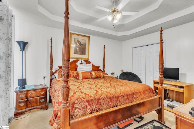 carpeted bedroom with a tray ceiling, a textured ceiling, a closet, and ceiling fan