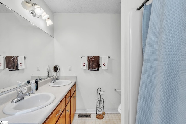 bathroom with vanity, toilet, curtained shower, and a textured ceiling