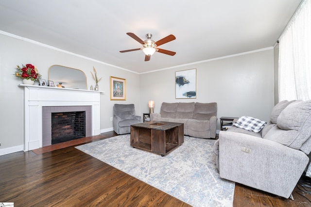 living room with a brick fireplace, crown molding, dark wood-type flooring, and ceiling fan