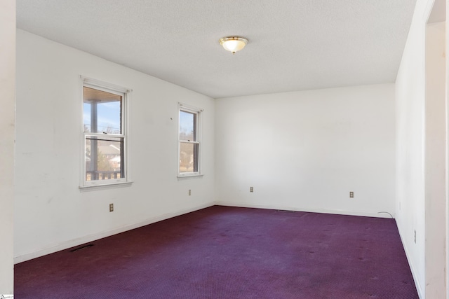 spare room with a textured ceiling and dark colored carpet