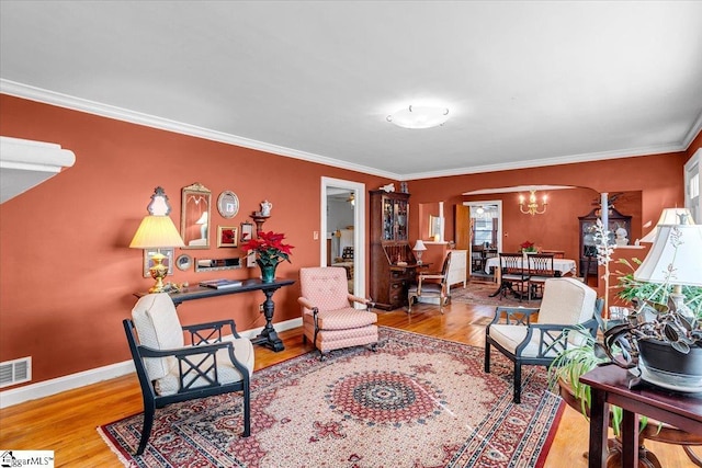 living room with an inviting chandelier, ornamental molding, and light hardwood / wood-style floors