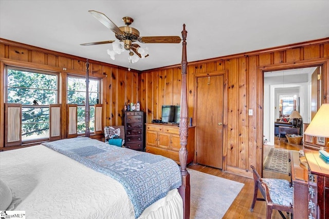 bedroom featuring ceiling fan, ornamental molding, light hardwood / wood-style flooring, and wood walls