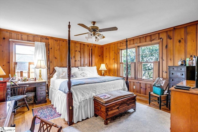 bedroom with multiple windows, wooden walls, ceiling fan, and light wood-type flooring