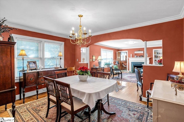 dining room featuring crown molding, a chandelier, light hardwood / wood-style flooring, and ornate columns