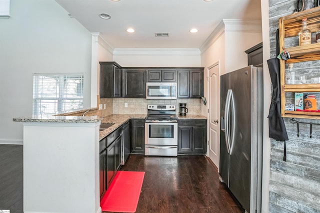 kitchen featuring sink, appliances with stainless steel finishes, kitchen peninsula, light stone countertops, and backsplash