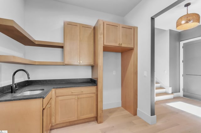 kitchen with hanging light fixtures, sink, light brown cabinets, and light wood-type flooring