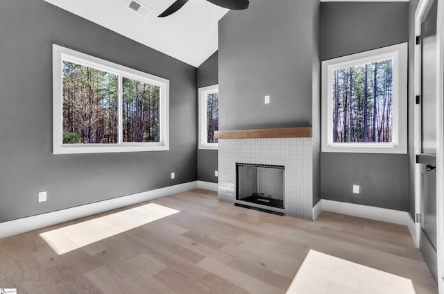 unfurnished living room with ceiling fan, high vaulted ceiling, a tile fireplace, and light wood-type flooring