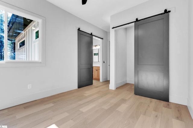 unfurnished bedroom with multiple windows, connected bathroom, a barn door, and light hardwood / wood-style flooring