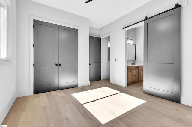 unfurnished bedroom featuring a barn door, sink, light hardwood / wood-style floors, and a closet