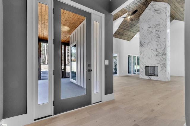 doorway with wood ceiling, high vaulted ceiling, a premium fireplace, and light hardwood / wood-style floors