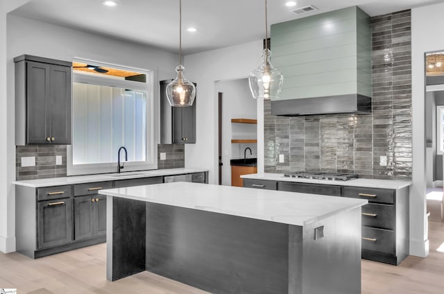 kitchen with sink, wall chimney range hood, appliances with stainless steel finishes, a center island, and light stone countertops