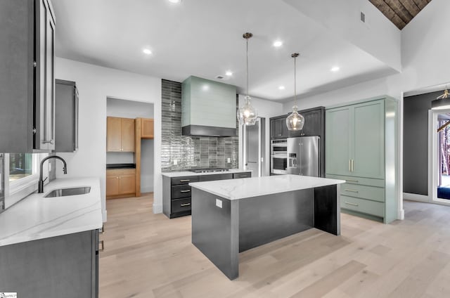 kitchen featuring wall chimney range hood, sink, appliances with stainless steel finishes, light stone countertops, and a kitchen island