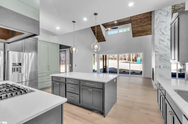 kitchen with gray cabinets, appliances with stainless steel finishes, light stone counters, a kitchen island, and decorative light fixtures