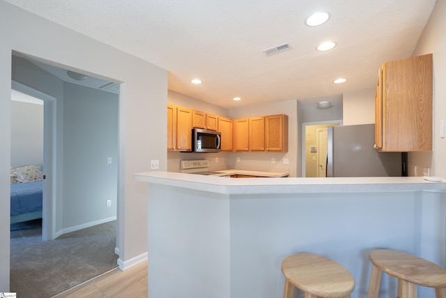 kitchen featuring appliances with stainless steel finishes, light brown cabinetry, a breakfast bar, and kitchen peninsula