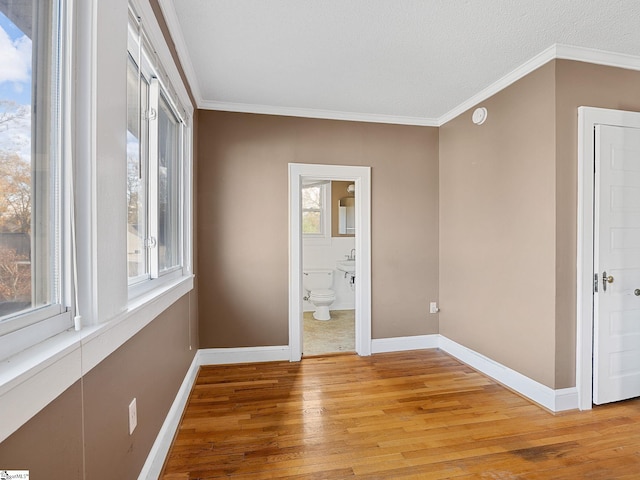 unfurnished bedroom with crown molding, connected bathroom, a textured ceiling, and light hardwood / wood-style flooring