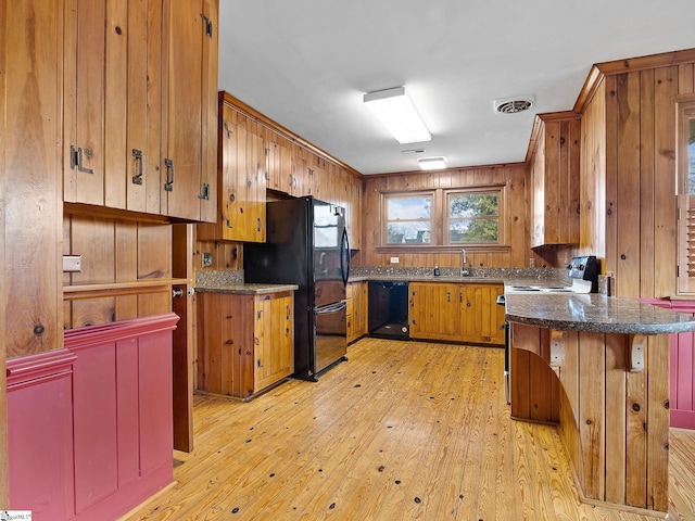 kitchen with sink, light hardwood / wood-style flooring, black appliances, and wood walls