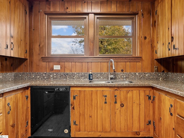 kitchen with wooden walls, black dishwasher, sink, and dark stone countertops