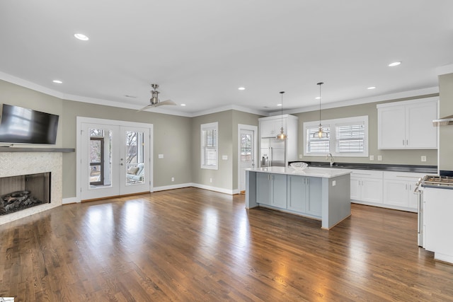 kitchen featuring white cabinetry, hanging light fixtures, stainless steel appliances, a center island, and a tiled fireplace