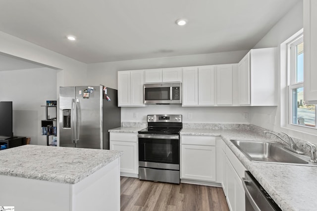 kitchen with stainless steel appliances, sink, white cabinets, and light hardwood / wood-style floors