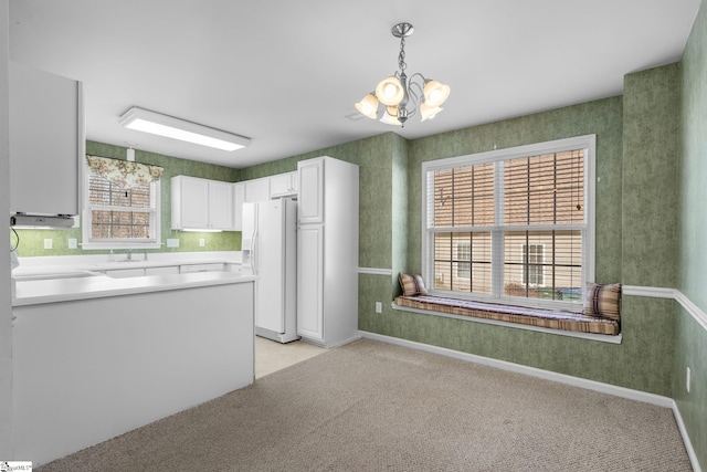 kitchen featuring an inviting chandelier, light carpet, pendant lighting, white refrigerator with ice dispenser, and white cabinets