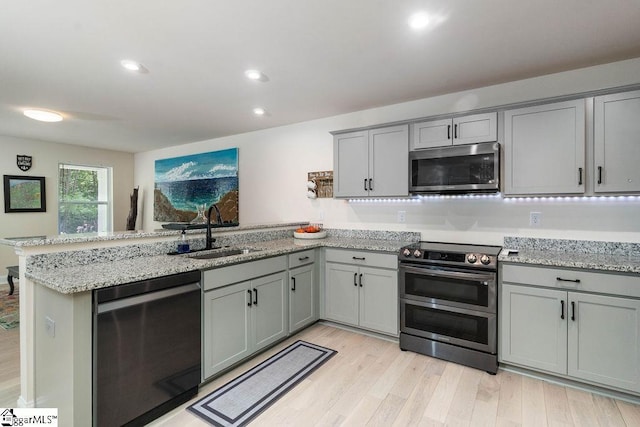 kitchen featuring sink, light hardwood / wood-style floors, kitchen peninsula, stainless steel appliances, and light stone countertops