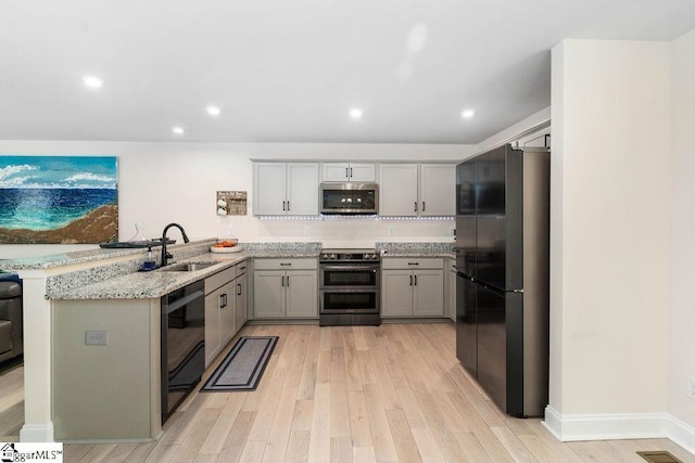 kitchen with black appliances, sink, light hardwood / wood-style floors, kitchen peninsula, and light stone countertops