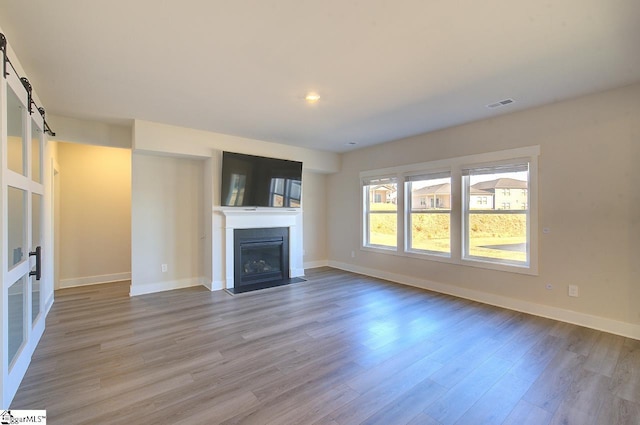 unfurnished living room with a barn door and light hardwood / wood-style flooring