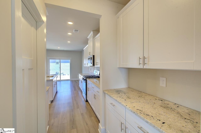 kitchen featuring light stone counters, light hardwood / wood-style flooring, white cabinets, stainless steel appliances, and backsplash