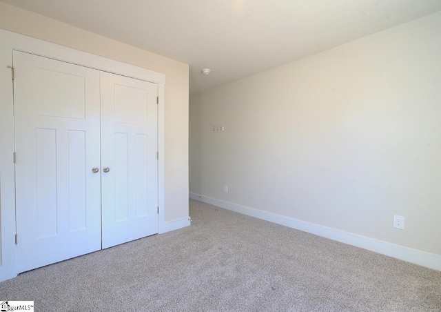 unfurnished bedroom with light colored carpet and a closet