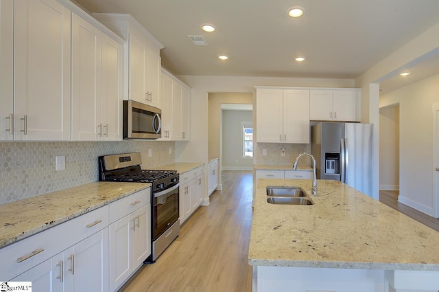 kitchen featuring sink, appliances with stainless steel finishes, white cabinetry, a kitchen island with sink, and light stone countertops